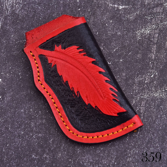 A handcrafted leather pouch or sheath featuring a bold red feather design embossed on a black leather background, with red leather trim and orange stitching, displayed on a dark textured surface.