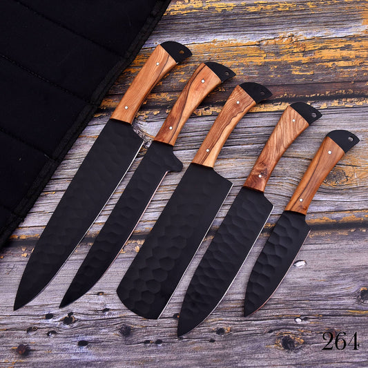 Five kitchen knives with black hammered blades and light brown wood handles are arranged diagonally on a rustic weathered wood surface next to a black carrying case.