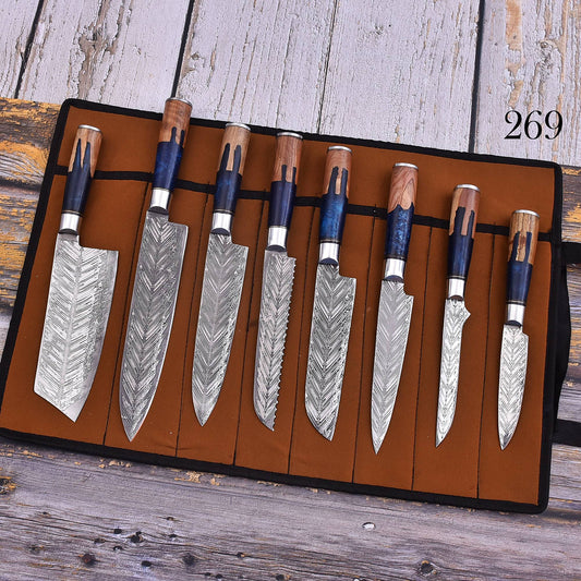 A set of eight kitchen knives with patterned Damascus steel blades and dark blue handles, displayed in a brown roll-up leather case on a rustic wooden surface. The number '269' is printed in black in the top right corner.