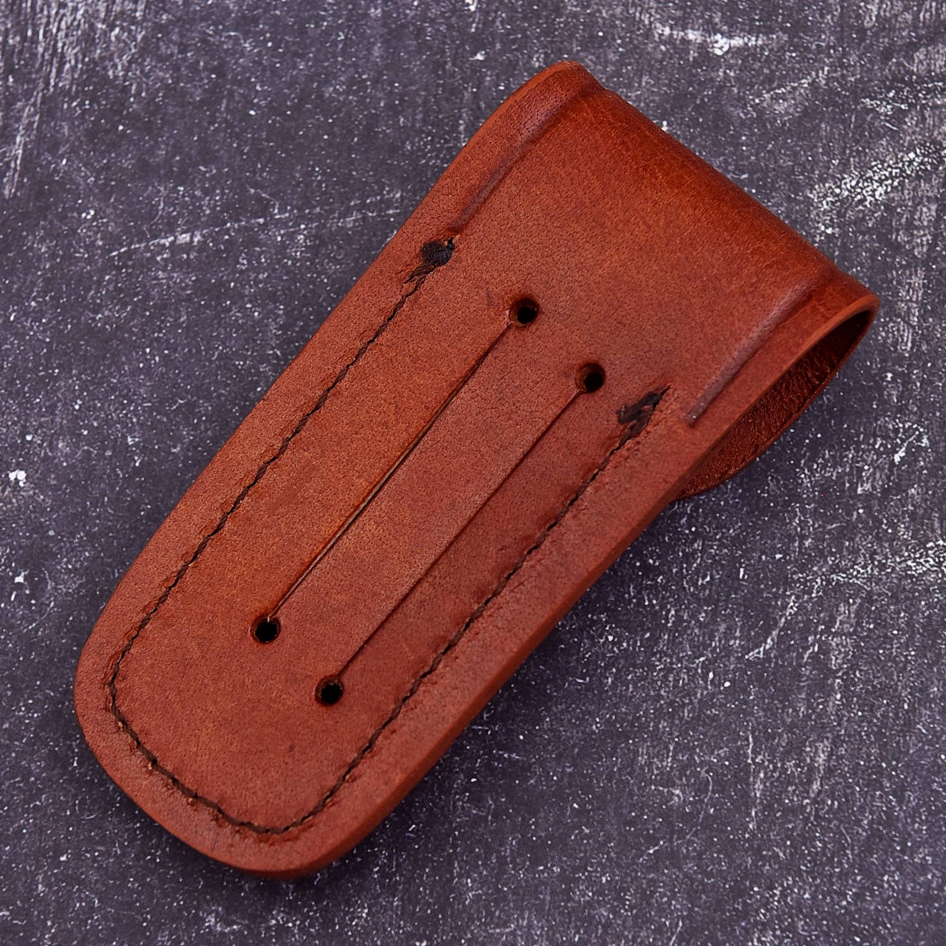 A brown leather money clip with double rows of stitching and three screw holes, shown on a textured dark gray background.