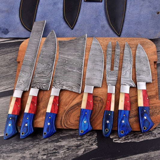 A set of seven Damascus steel kitchen knives with patriotic red, white, and blue handles, arranged on a wooden cutting board with a blue leather sheath in the background.