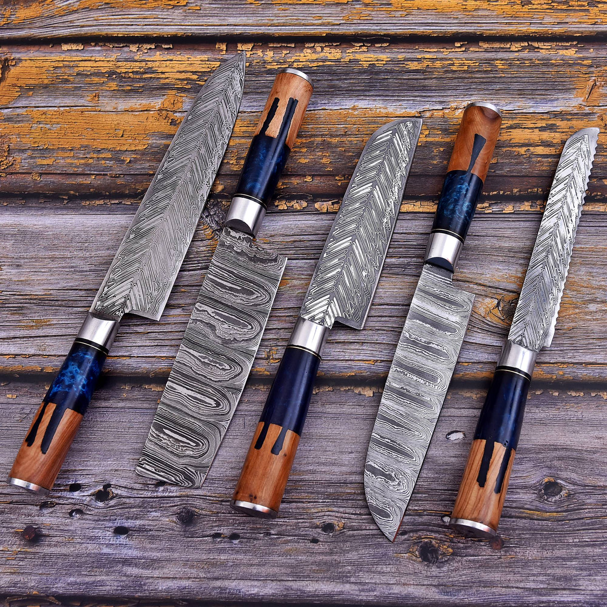 Five kitchen knives with patterned steel blades and dark blue/black and brown wooden handles arranged on a rustic wooden surface.