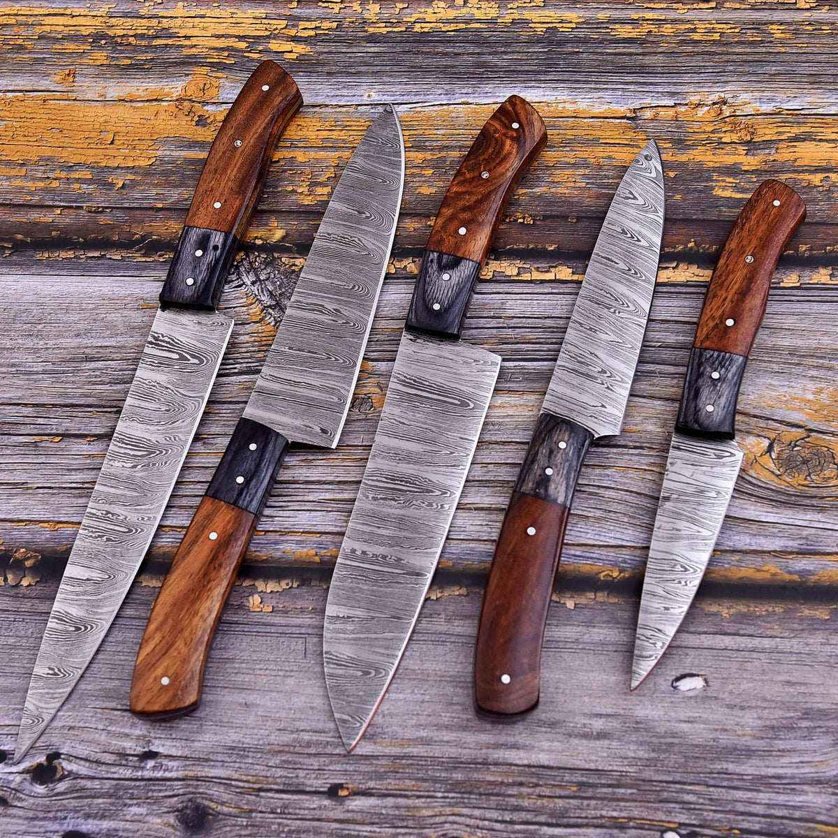 Five kitchen knives with patterned steel blades and wooden handles arranged on a rustic weathered wood surface.