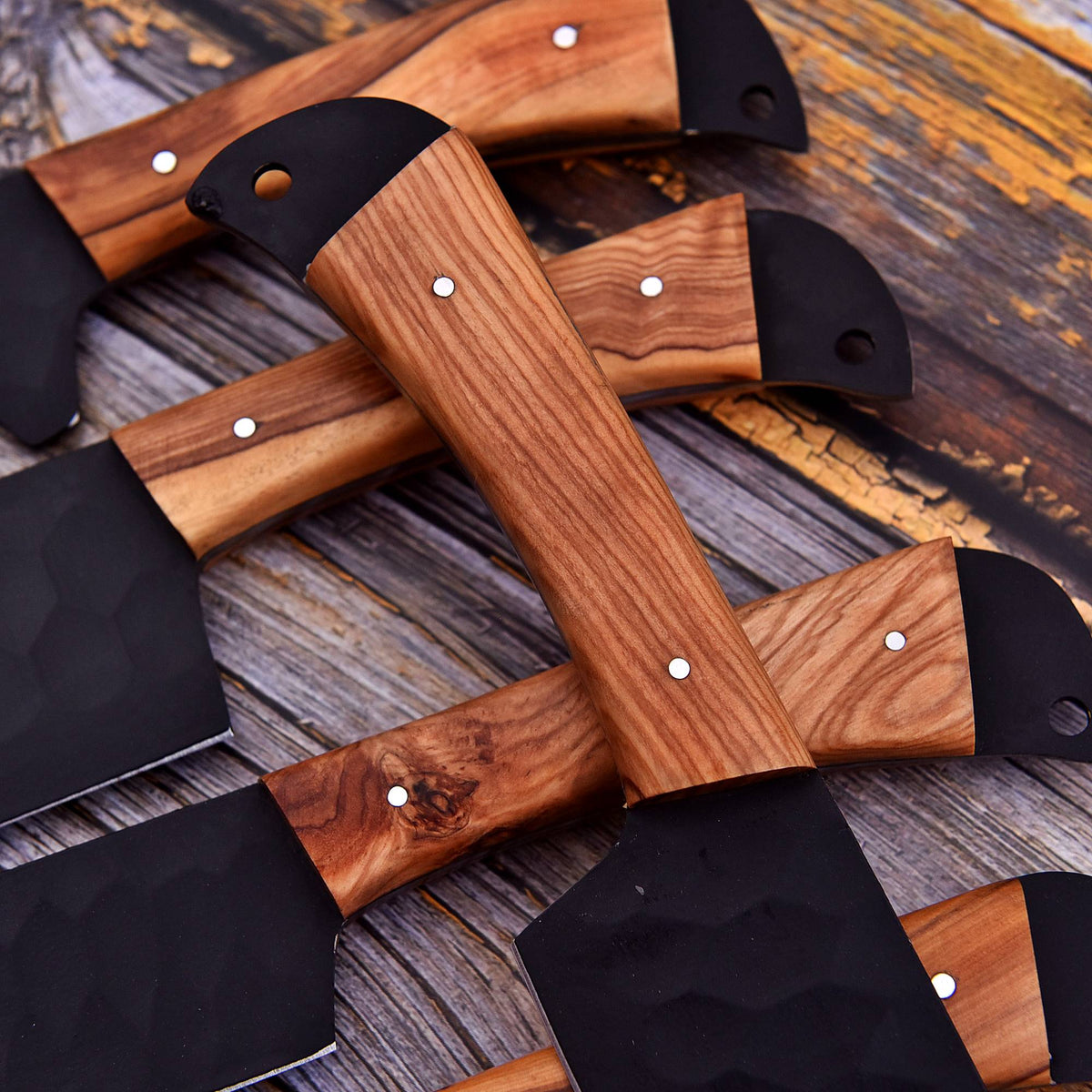 Several hand axes with polished wood handles and black metal blades are arranged on a rustic wooden surface.