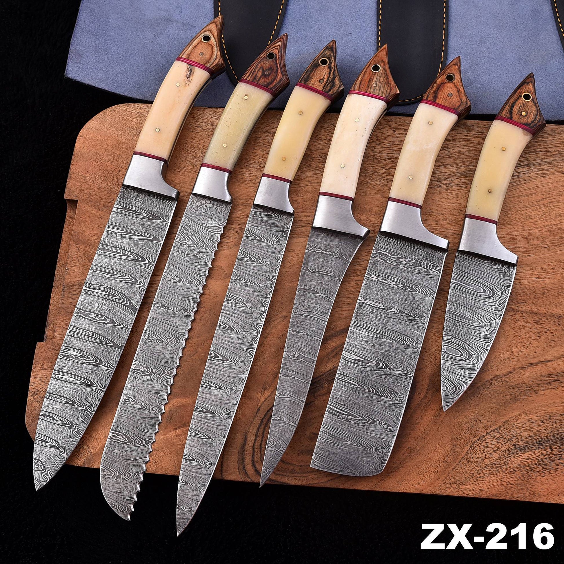 Six kitchen knives with patterned Damascus steel blades and cream-colored handles with reddish-brown wooden end caps, arranged on a wooden cutting board with a dark background and a blue pouch behind them. The text 'ZX-216' appears in the bottom right corner.