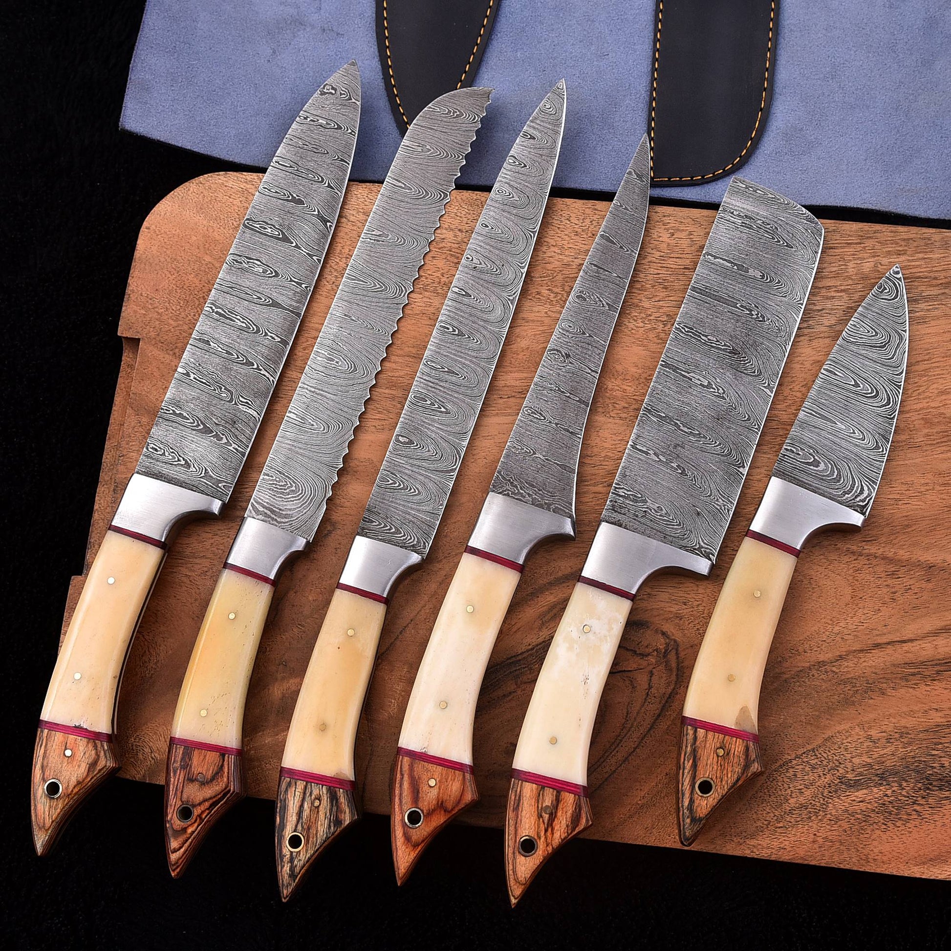 Six-piece handmade Damascus kitchen knife set with light bone and wood handles, including a bread knife, cleaver and chef knives