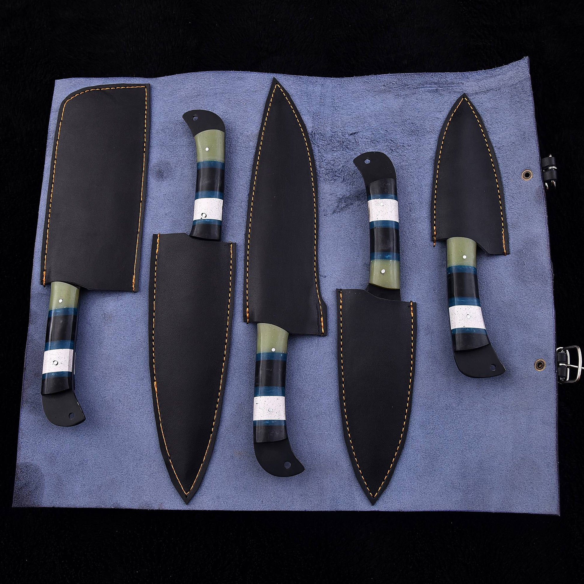 Five fixed-blade knives with black leather sheaths arranged on a blue fabric roll against a black background.