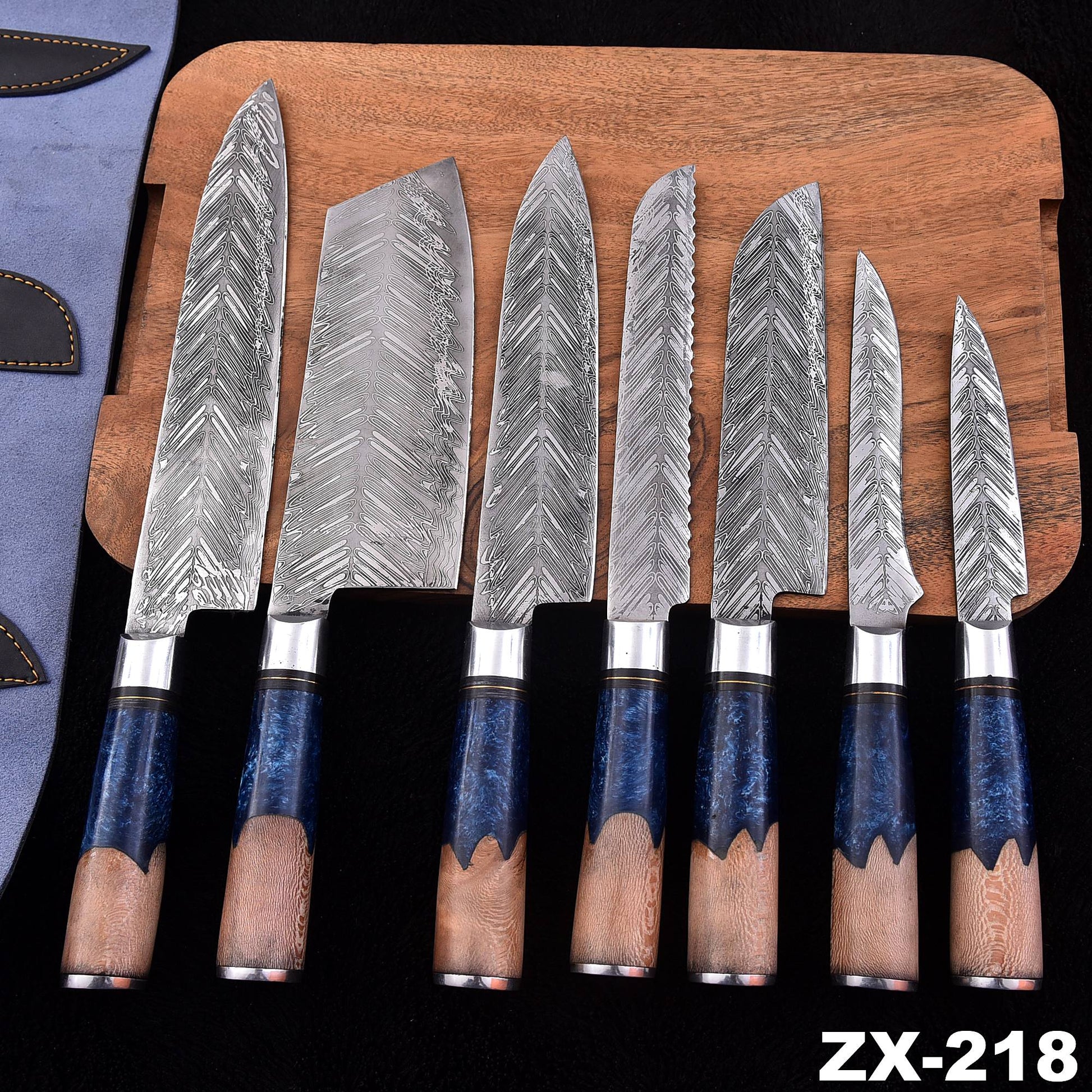 A set of seven kitchen knives with patterned steel blades and dark blue handles with natural wood grips, displayed on a wooden cutting board over a black background.