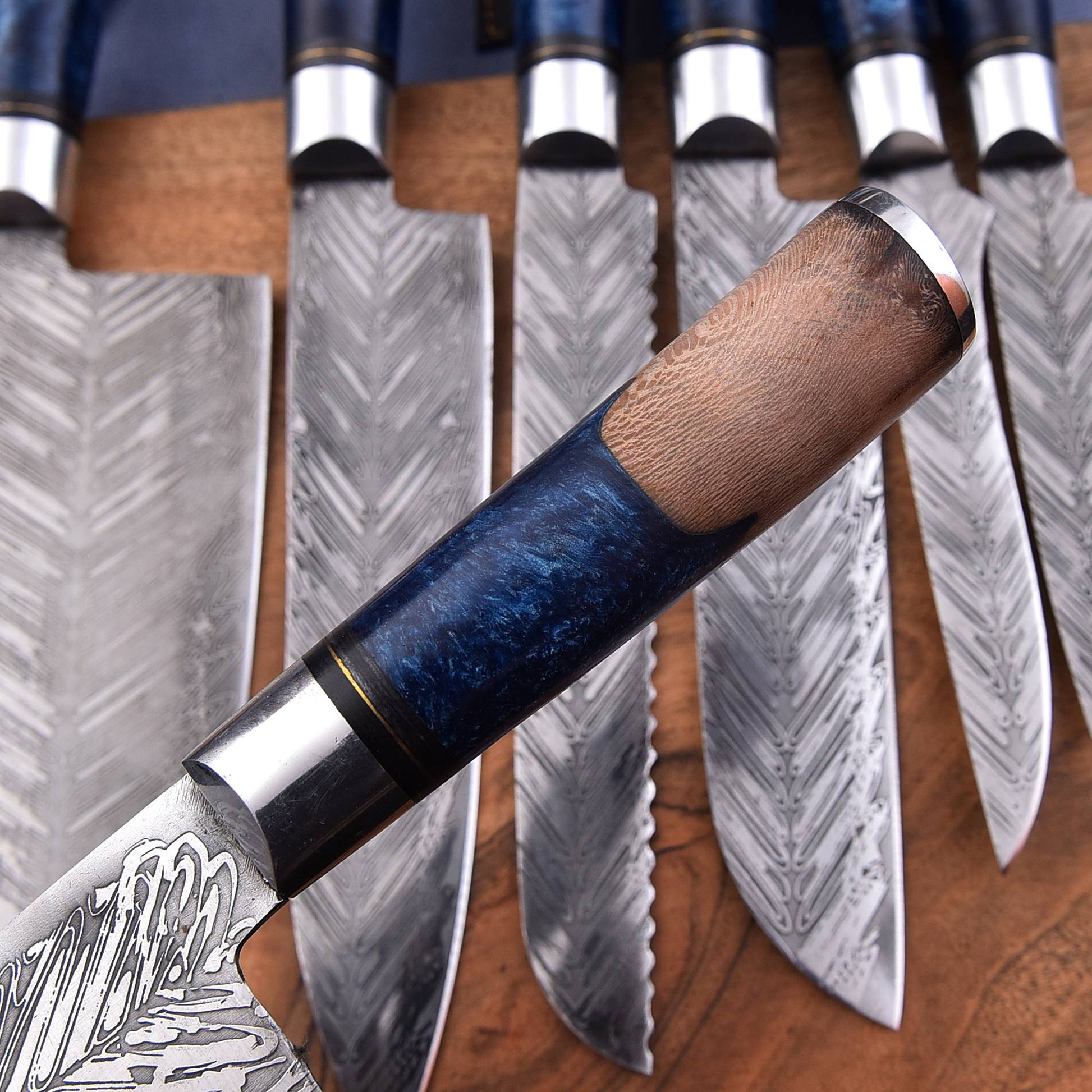 A close-up of a kitchen knife with a patterned steel blade and a dark blue wood handle with a brown grip, displayed in front of a set of similar knives on a wooden surface.