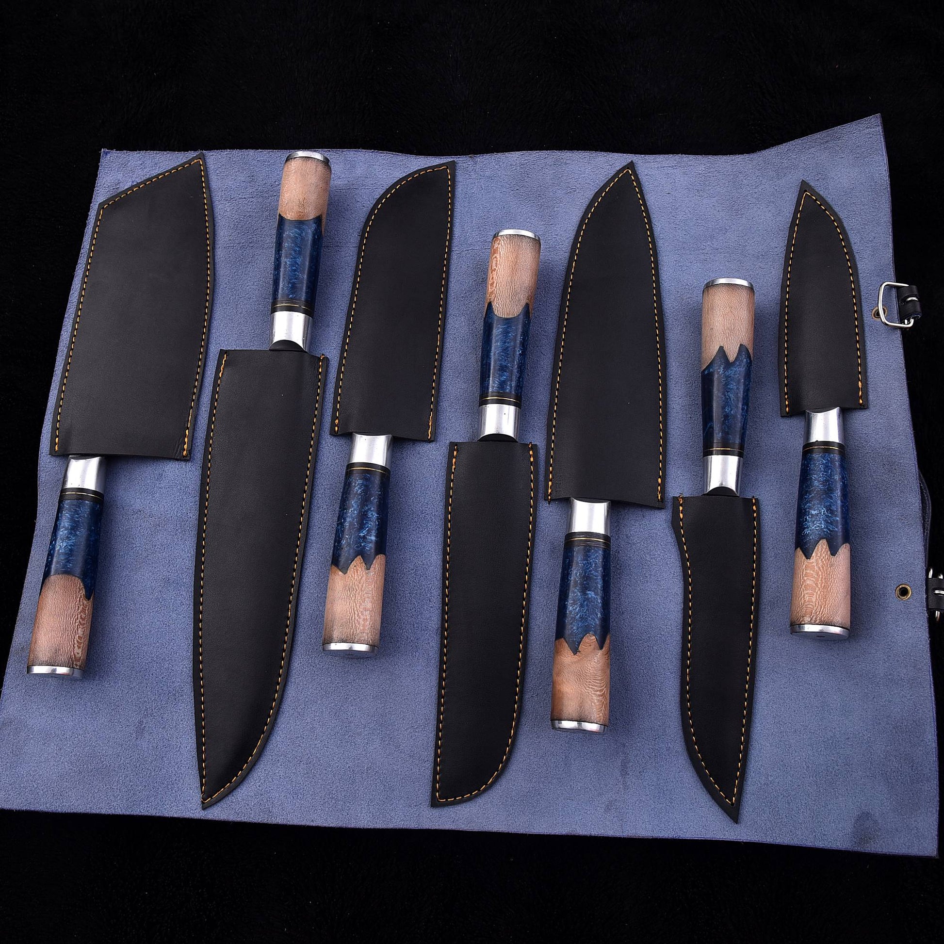 A set of six kitchen knives with blue marbled handles and black leather sheaths, displayed on a blue fabric roll against a black background.