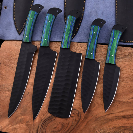 Five kitchen knives with black hammered blades and green marbled handles are arranged on a wooden surface with a blue knife sheath behind them.