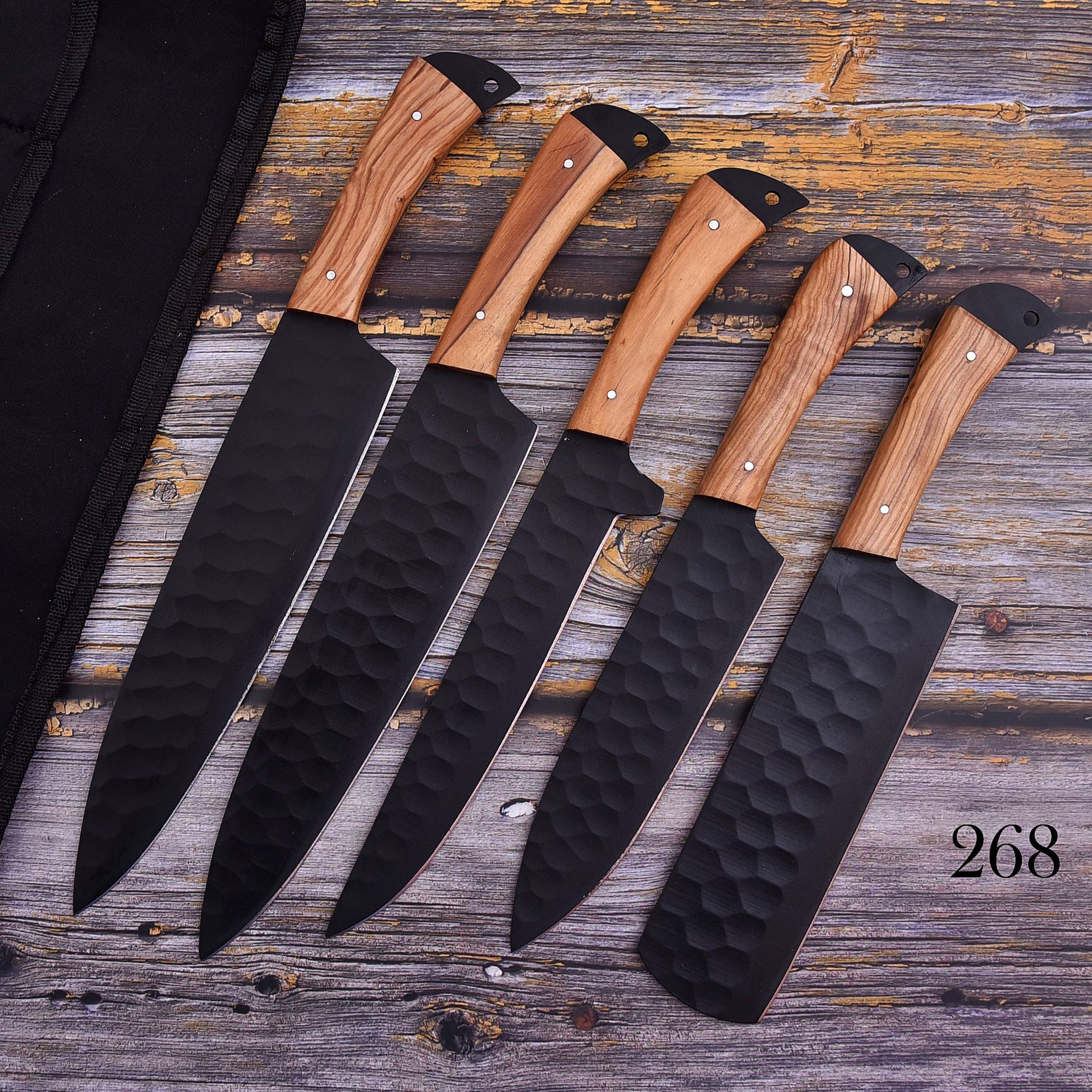 Five kitchen knives with hammered black blades and light brown wood handles are arranged diagonally on a rustic weathered wood surface next to a black knife sheath. The number 268 is printed in the bottom right corner.