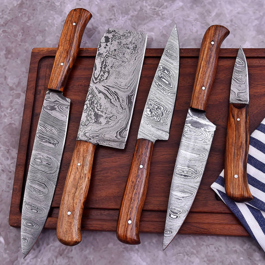Five Damascus steel kitchen knives with dark wood handles arranged on a dark wooden cutting board over a gray stone surface.