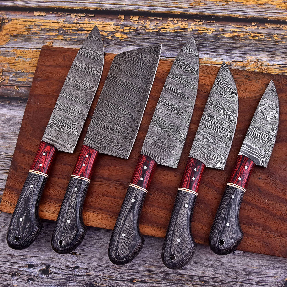 Set of five Damascus knives with red handles on a wooden cutting board.