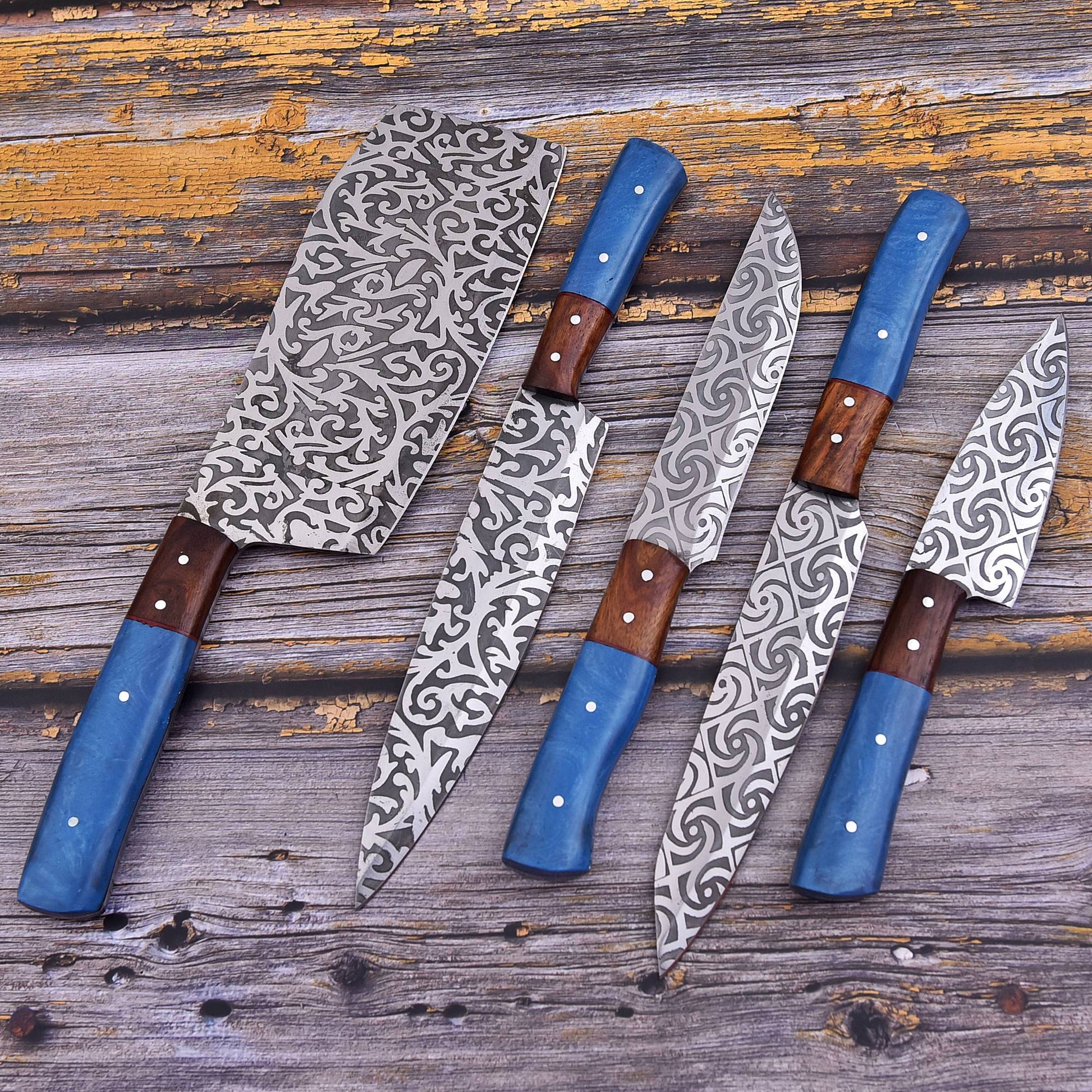 Five kitchen knives and a cleaver arranged on a rustic weathered wood surface. The knives feature patterned silver steel blades, blue handles, and brown wooden bolsters.