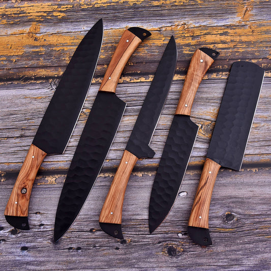 Five kitchen knives with black hammered blades and light brown wood handles arranged diagonally on a rustic weathered wood background.