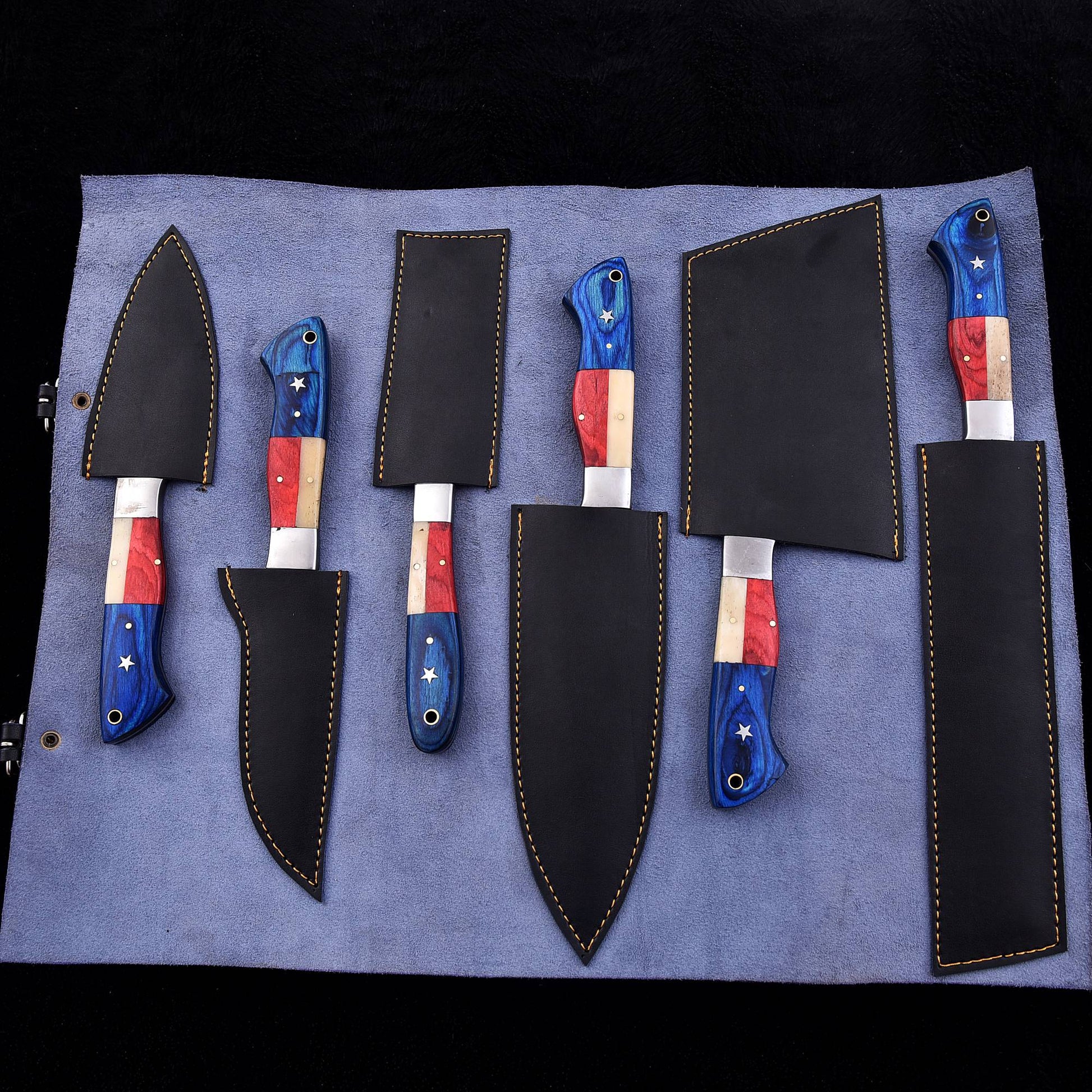 A set of six kitchen knives with patriotic red, white, and blue handles, displayed on a blue roll-up leather sheath against a black background.