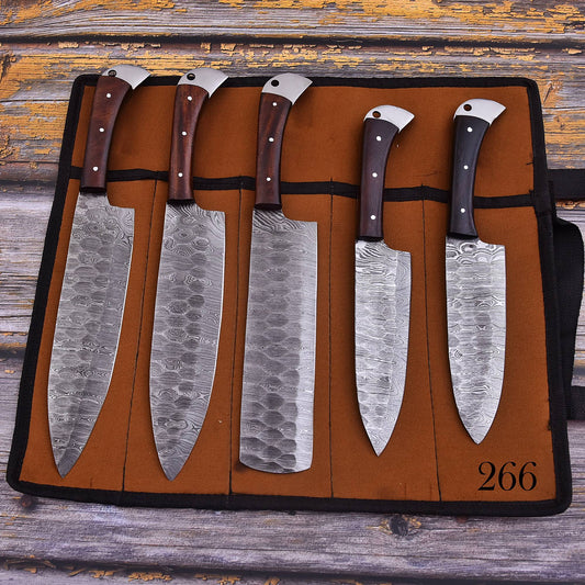 Five kitchen knives with patterned steel blades and dark wooden handles, displayed in a brown leather knife roll on a rustic wooden surface.