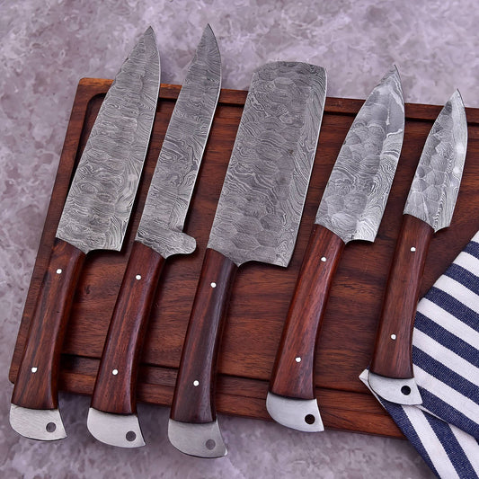 Five Damascus steel kitchen knives with dark brown wooden handles arranged on a wooden cutting board over a gray stone surface, with a striped cloth partially visible at the lower right.