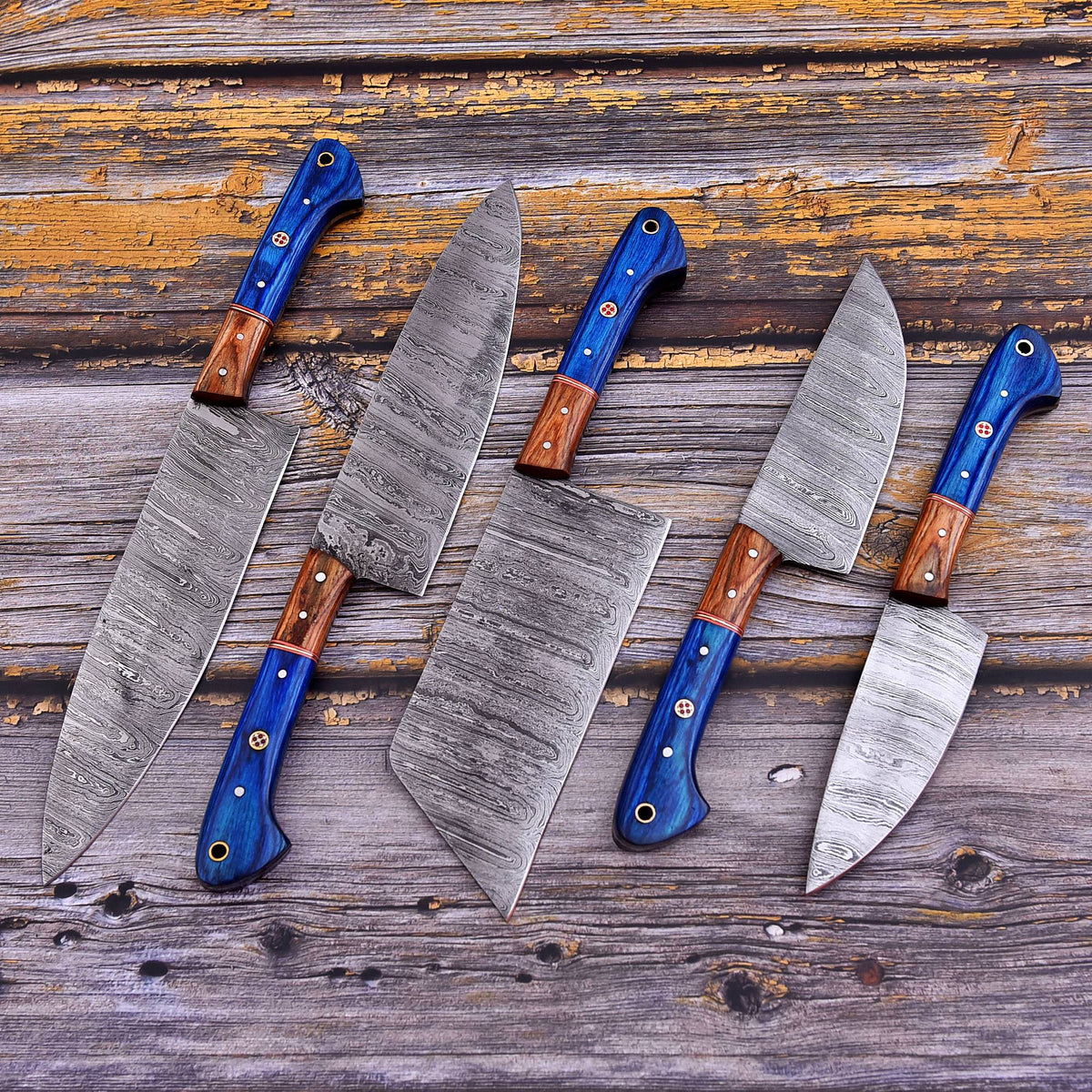 Five kitchen knives with patterned steel blades and blue handles with brown wooden sections, arranged on a rustic weathered wood surface.