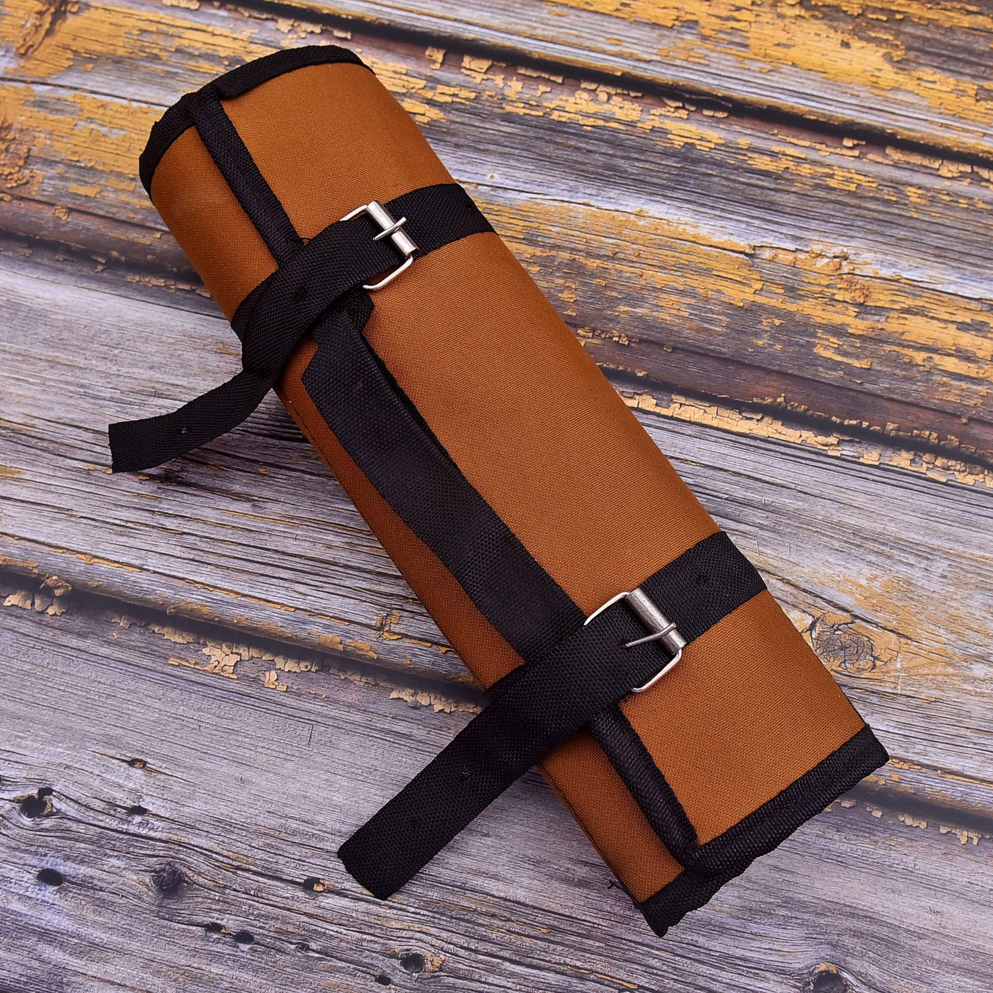 A rolled brown yoga mat secured with black straps and silver buckles, placed diagonally on a rustic weathered wood plank surface.