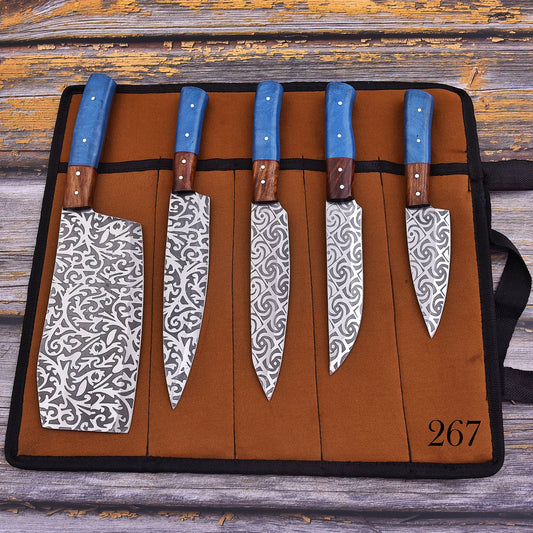 Five kitchen knives with patterned steel blades and blue handles are displayed in a brown knife roll on a rustic wooden surface. The knife roll has a black strap and the number 267 printed in the bottom right corner.