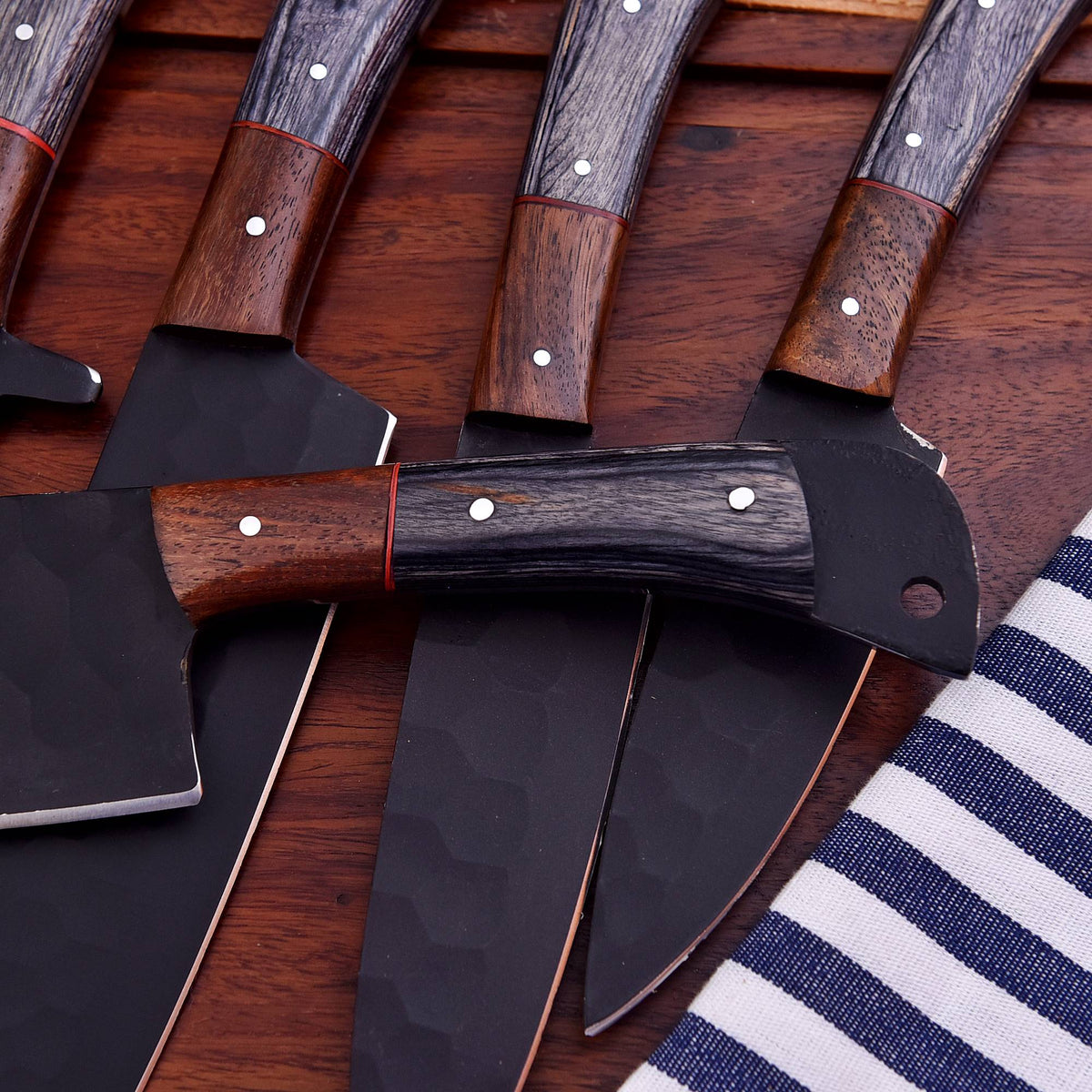 A set of outdoor survival and hunting tools, including a hatchet and knives, arranged on a dark wooden surface with a blue and white striped fabric in the corner.